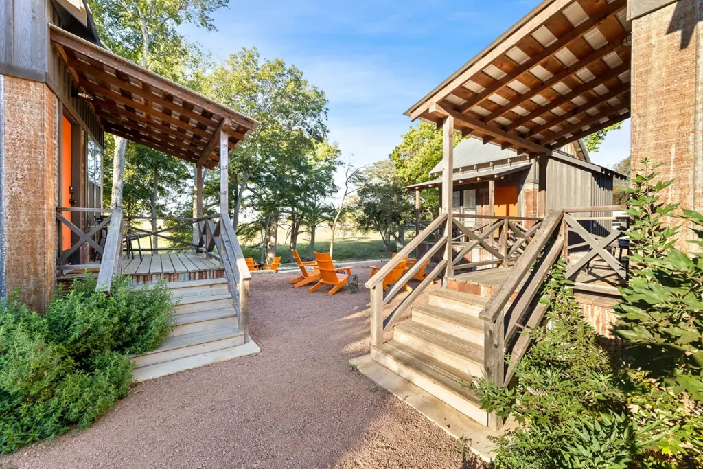Rustic cabins with wooden porches and a courtyard featuring bright orange Adirondack chairs at Camp Comfort.