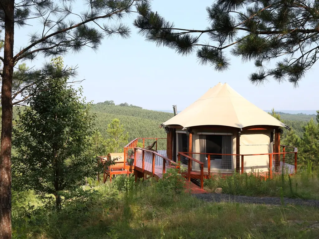Luxury canvas glamping yurt with a spacious wooden deck on a forested hillside at a nature immersive resort.
