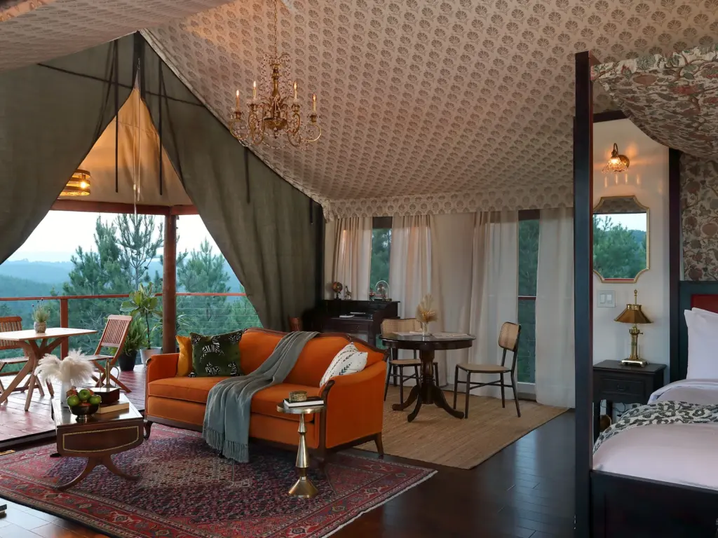 Elegant glamping tent interior featuring a patterned ceiling, chandelier, orange velvet sofa, and a four-poster bed at a nature immersive resort.
