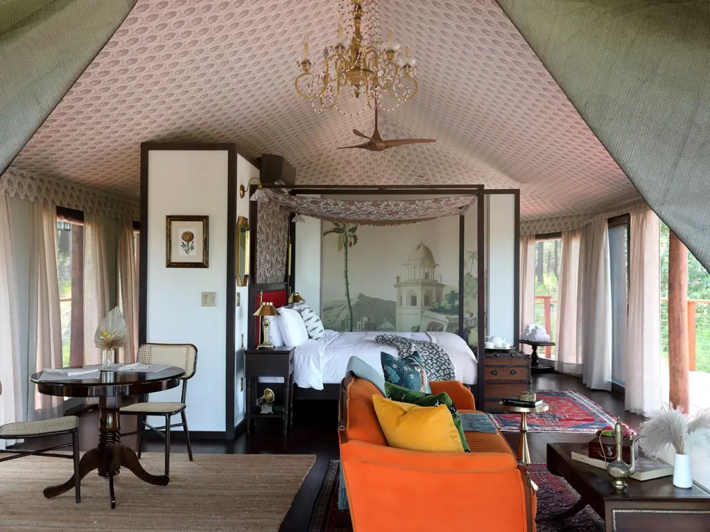 Spacious luxury tent interior showcasing a canopy bed with a landscape mural, a vintage seating area, and panoramic forest views.