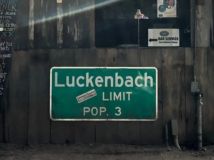 The iconic green Luckenbach Limit Pop 3 sign mounted on a weathered wooden wall.