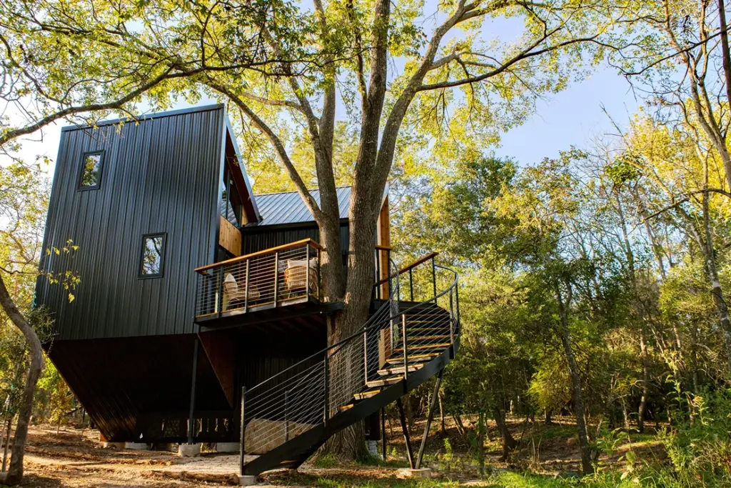 Modern black treehouse cabin with a spiral staircase built around a large tree at Onera Fredericksburg.