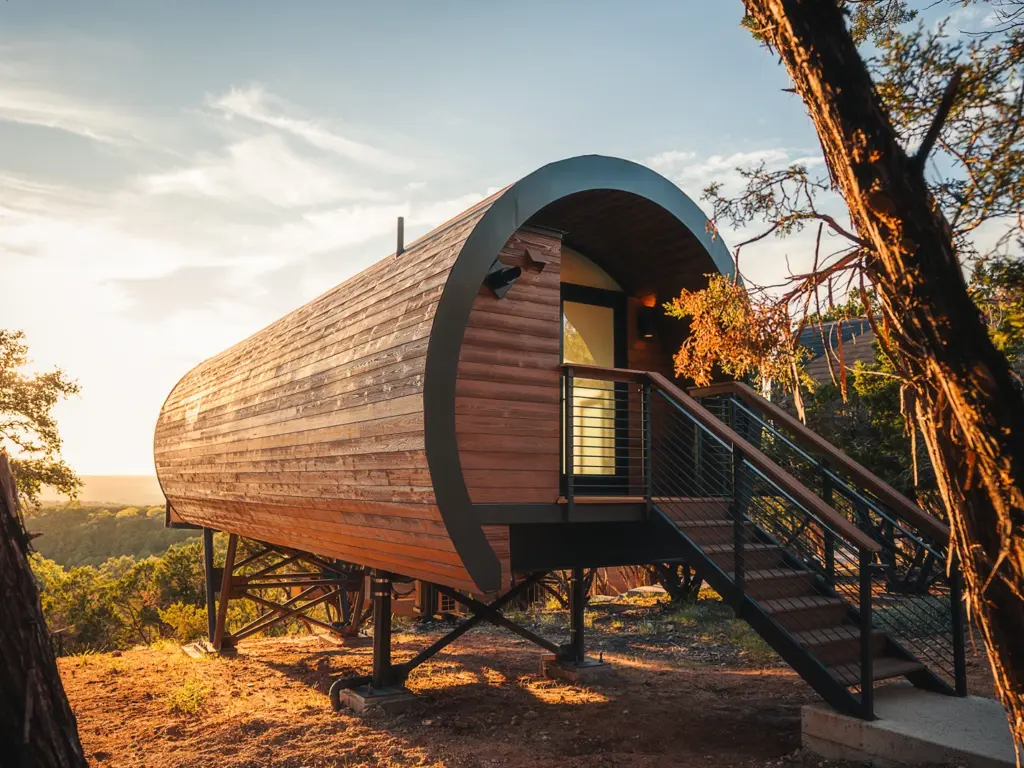 Unique barrel-shaped wooden cabin elevated on metal stilts at sunset at a nature immersive resort.