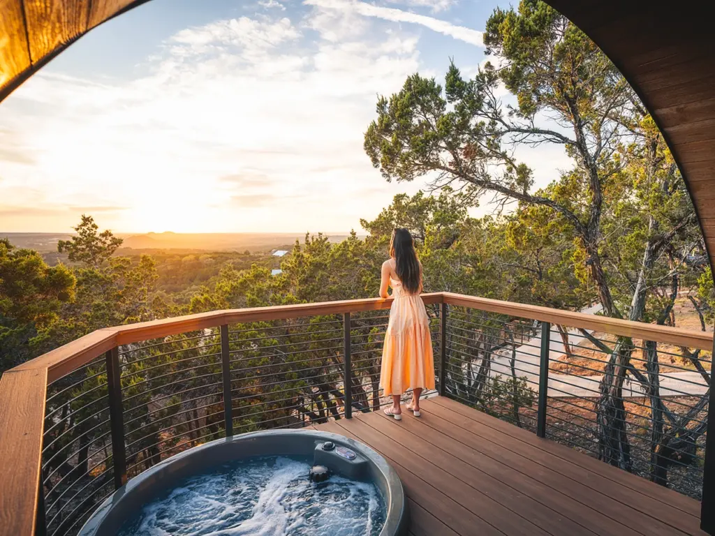 Woman enjoying a sunset view from a balcony with a hot tub at one of the luxury Wimberley TX Cabins.
