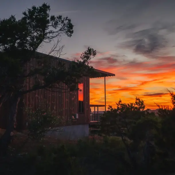 Modern wood cabin exterior at Onera against a vibrant orange sunset.