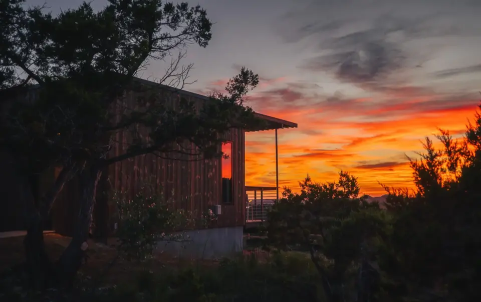 Modern wood cabin exterior at Onera against a vibrant orange sunset.