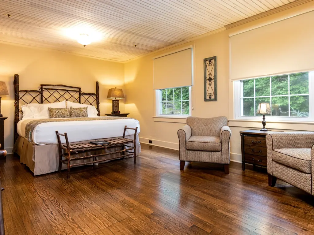 Cozy rustic bedroom interior featuring a custom log bed, hardwood floors, and comfortable armchairs by a bright window.