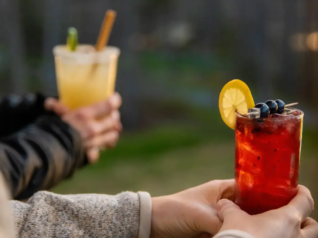 Close-up of guests holding a refreshing red berry cocktail and a yellow mixed drink outdoors at a nature immersive resort.