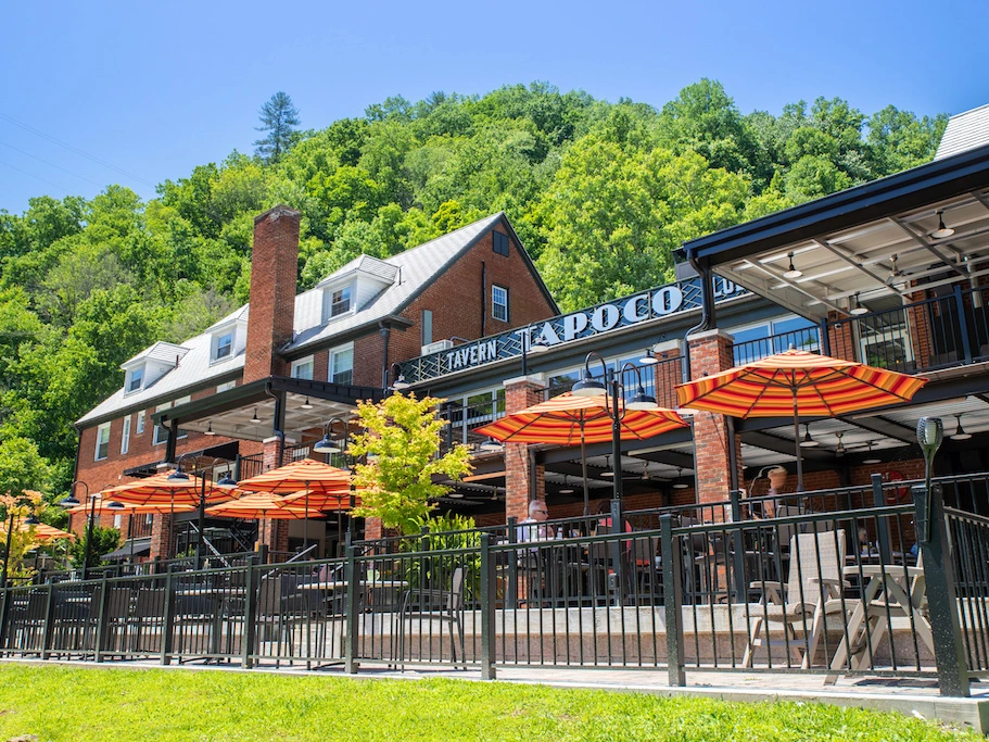Ground-level view of a brick tavern's outdoor dining patio featuring patio tables shaded by bright orange umbrellas.