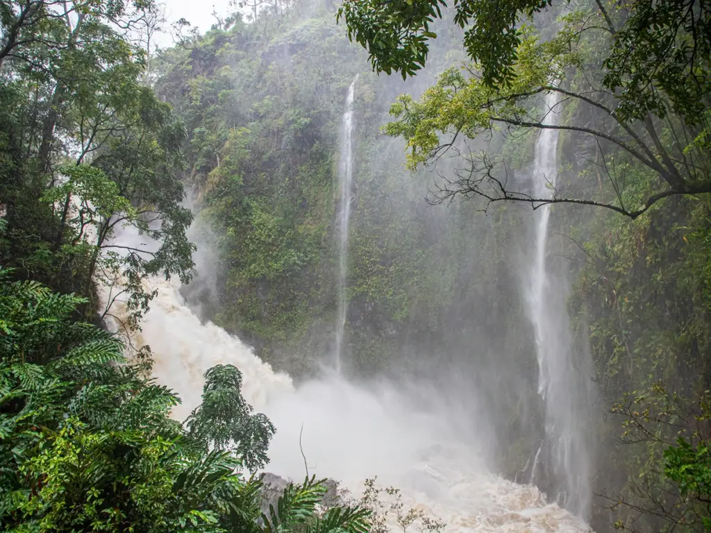 tall waterfall cascading into a rocky river, surrounded by dense green trees and mist. Best time to visit Big Island