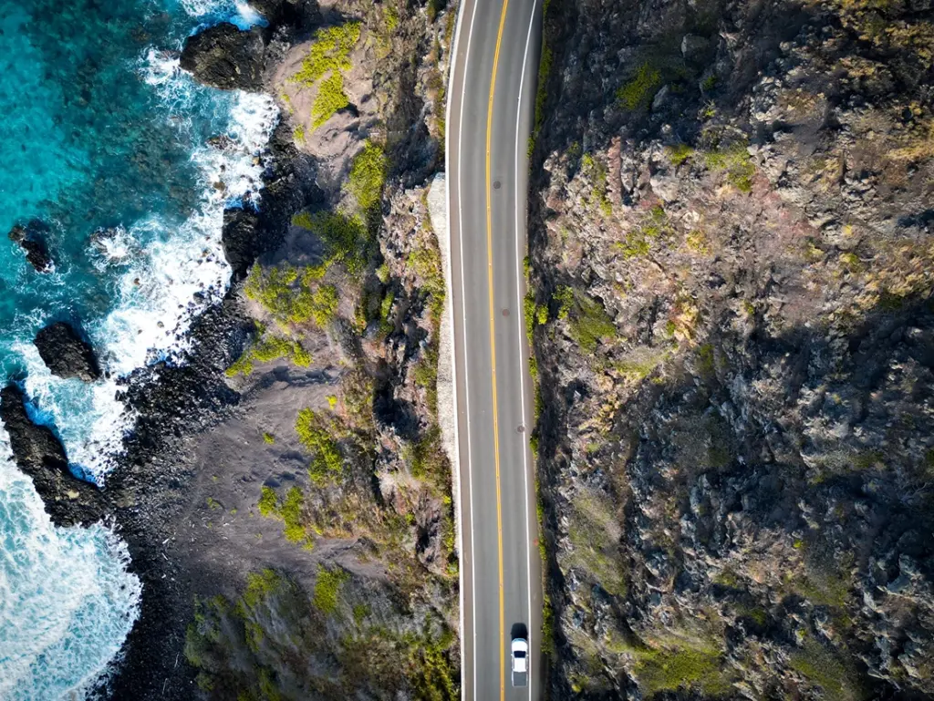 Aerial view of a winding road along a rocky coastline with waves crashing.