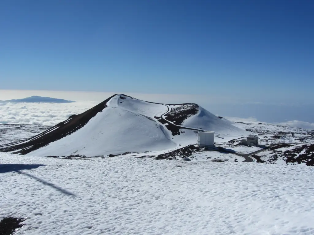 Snow-covered volcano peaks against a clear blue sky, with a road and buildings below. - Best Time to Visit Big Island