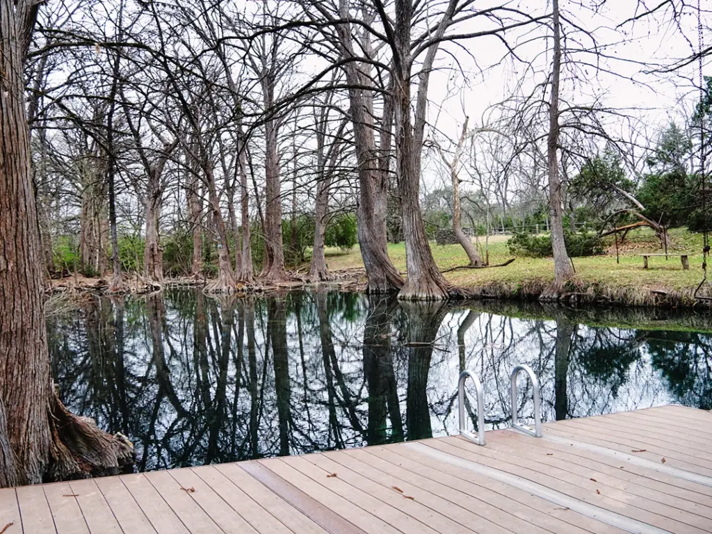Clear water reflecting cypress trees at Blue Hole in Wimberley, a must-visit spot on a texas travel itinerary.