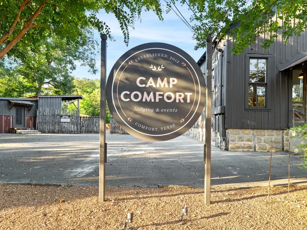 A round black sign for Camp Comfort lodging in Texas, a scenic stop to include on a texas travel itinerary.