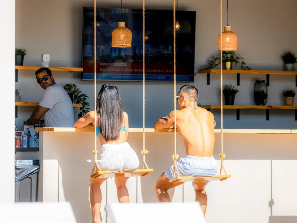 A couple sitting on wooden swing seats at an outdoor bar counter with hanging lamps at The Cedars Ranch.