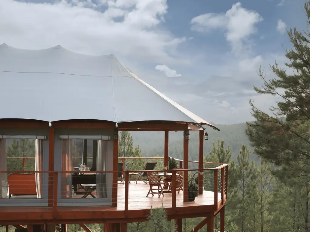 Exterior of luxury safari tents southeast usa, featuring a spacious wooden deck overlooking a misty pine forest.