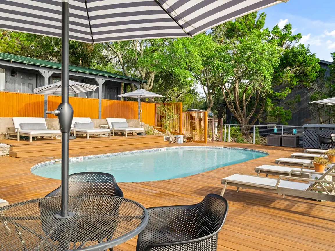Swimming pool with lounge chairs and striped umbrellas at The Bygone, offering boutique Wimberley TX Cabins
