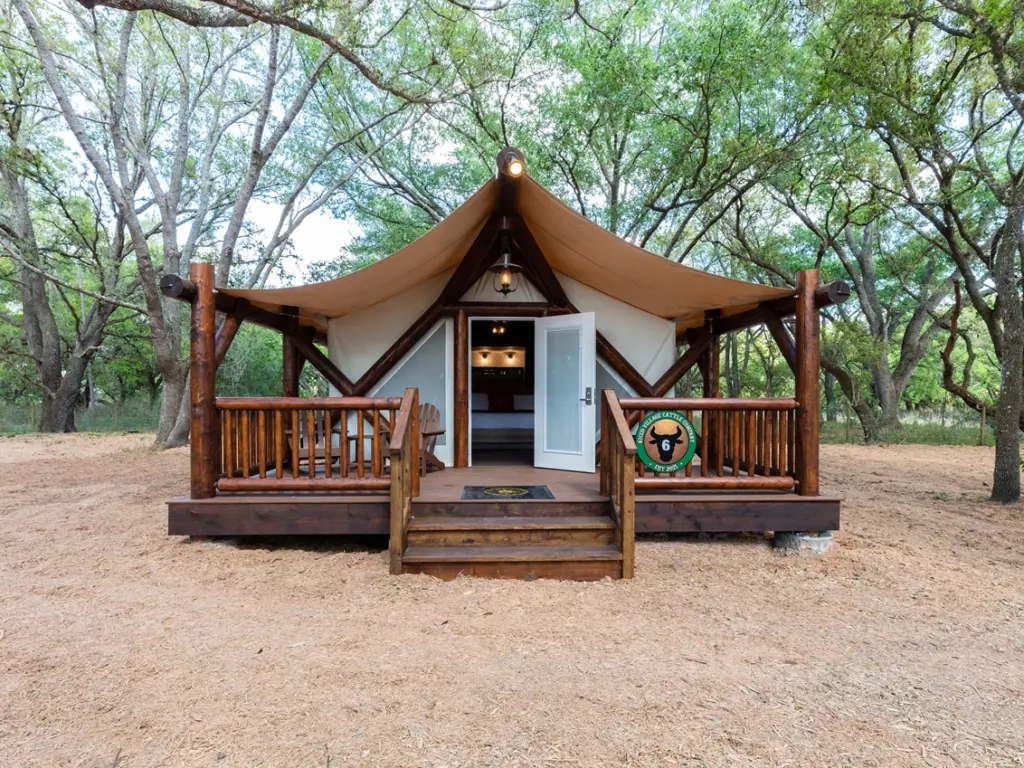 Exterior of luxury safari tents southeast usa with a log frame and small front porch surrounded by trees.