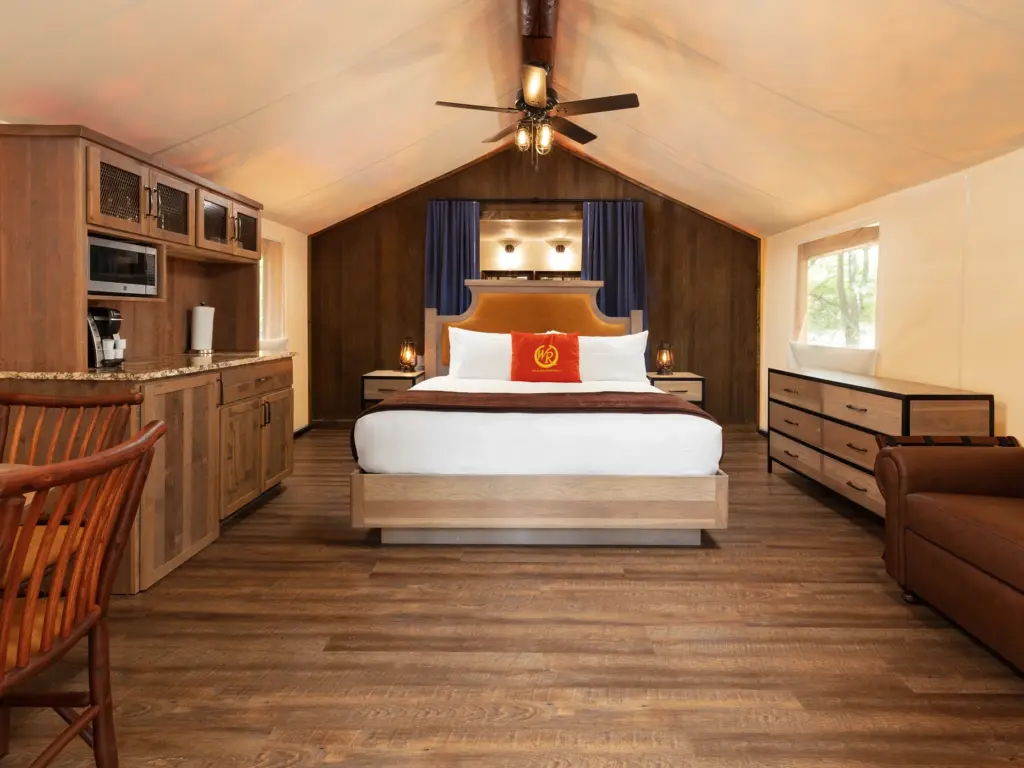 nterior of a glamping tent with a large bed, wooden kitchenette, and leather furniture under a canvas roof.