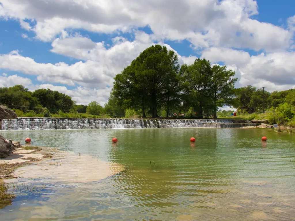 Water cascading over a low dam on the blanco river with orange buoys in the foreground.