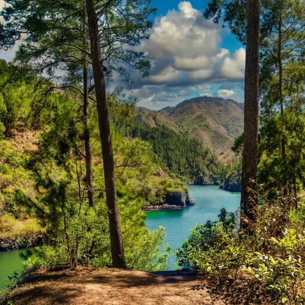 A scenic view of the winding blanco river nestled between steep, pine-covered hills under a blue sky.
