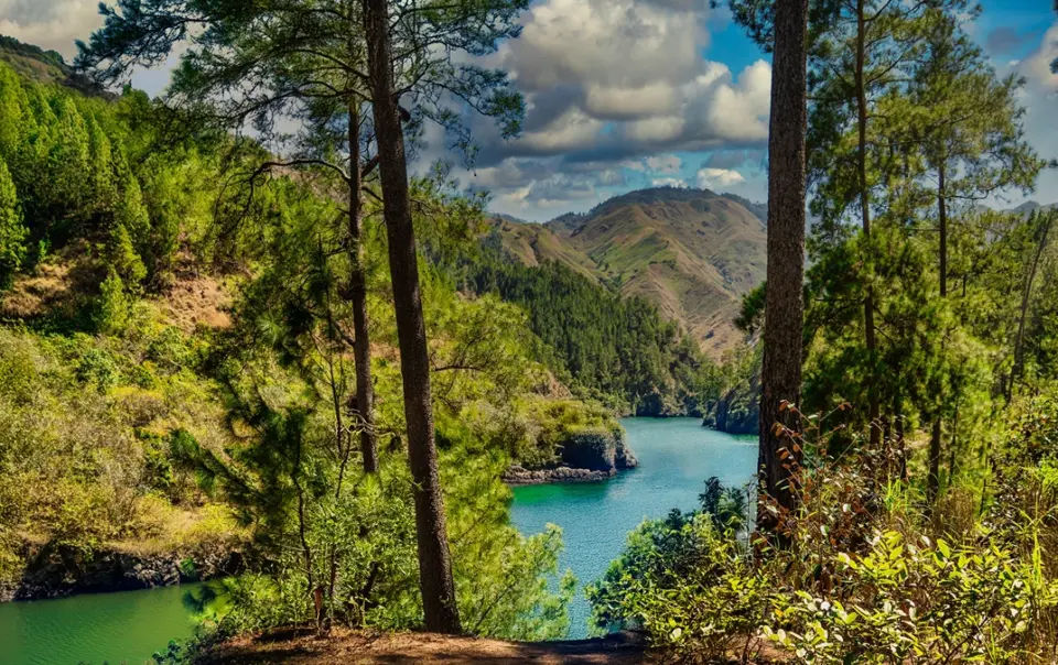 A scenic view of the winding blanco river nestled between steep, pine-covered hills under a blue sky.