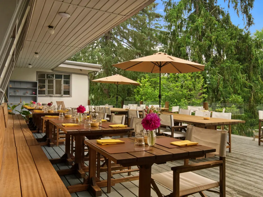 Upscale wilderness retreats northeast feature wooden outdoor dining tables with yellow napkins on a patio deck.