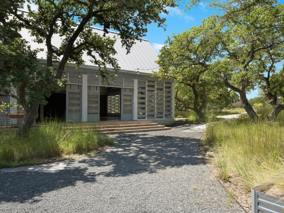 Modern eco-conscious event barn with gray wood siding and sliding doors nestled among mature oak trees.