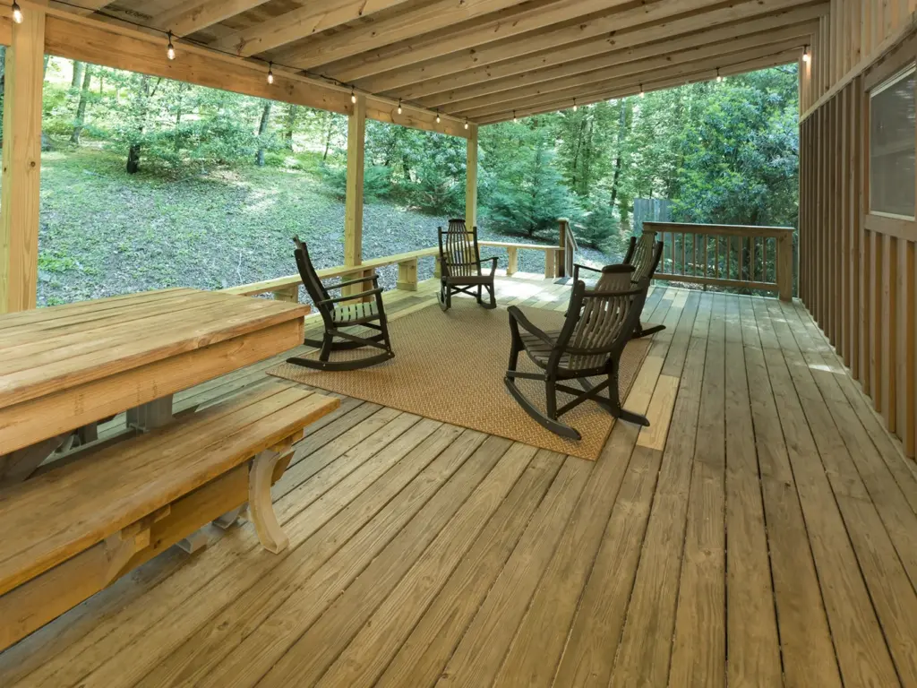 A large wooden deck featuring rocking chairs and a picnic table at Huffman Creek Retreat.