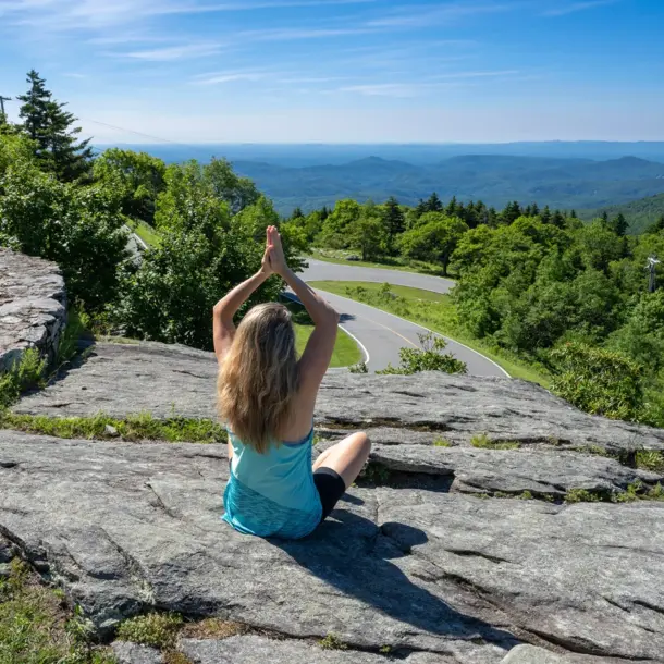 A woman meditating on a Blue Ridge Parkway rock overlook, capturing the spirit of secluded yoga retreats north carolina.