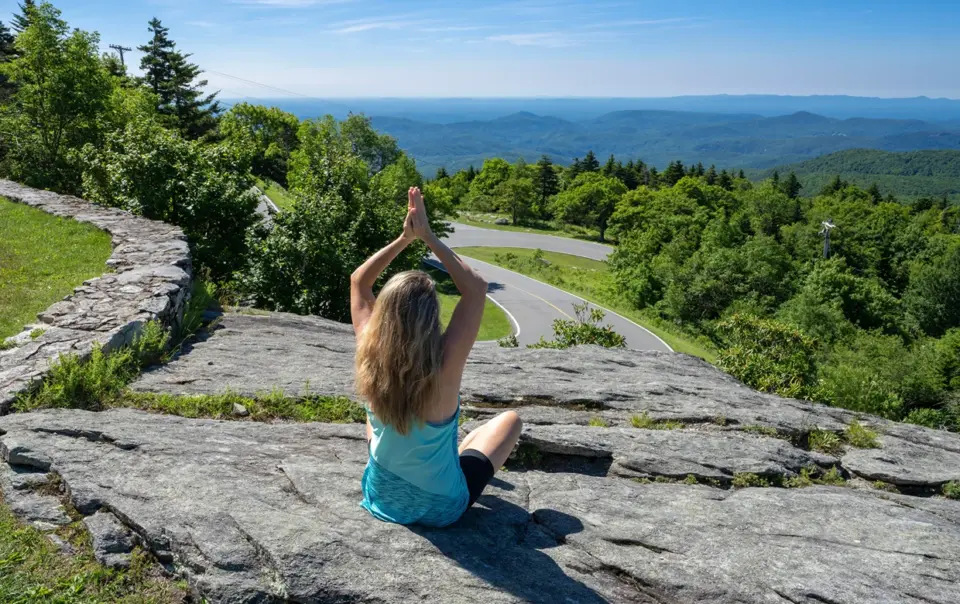 A woman meditating on a Blue Ridge Parkway rock overlook, capturing the spirit of secluded yoga retreats north carolina.