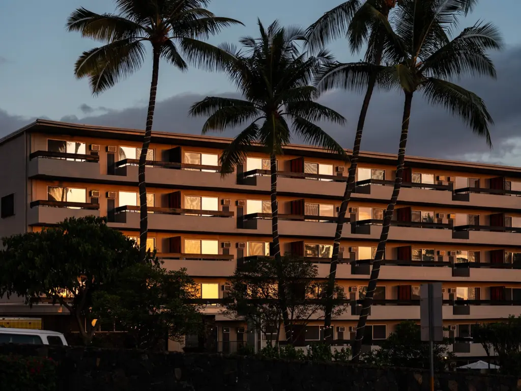 Sunset view of a multi-story building and palm trees at Pacific 19, one of the design hotels kailua kona.