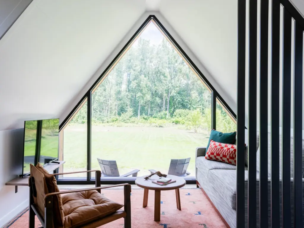 Indoor view of a contemporary A-frame cabin living room looking out a large triangular window onto a lawn.