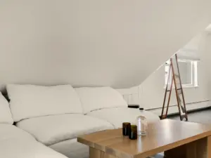 A bright attic living space with a white sectional sofa, wood coffee table, and a lean ladder near a small window.