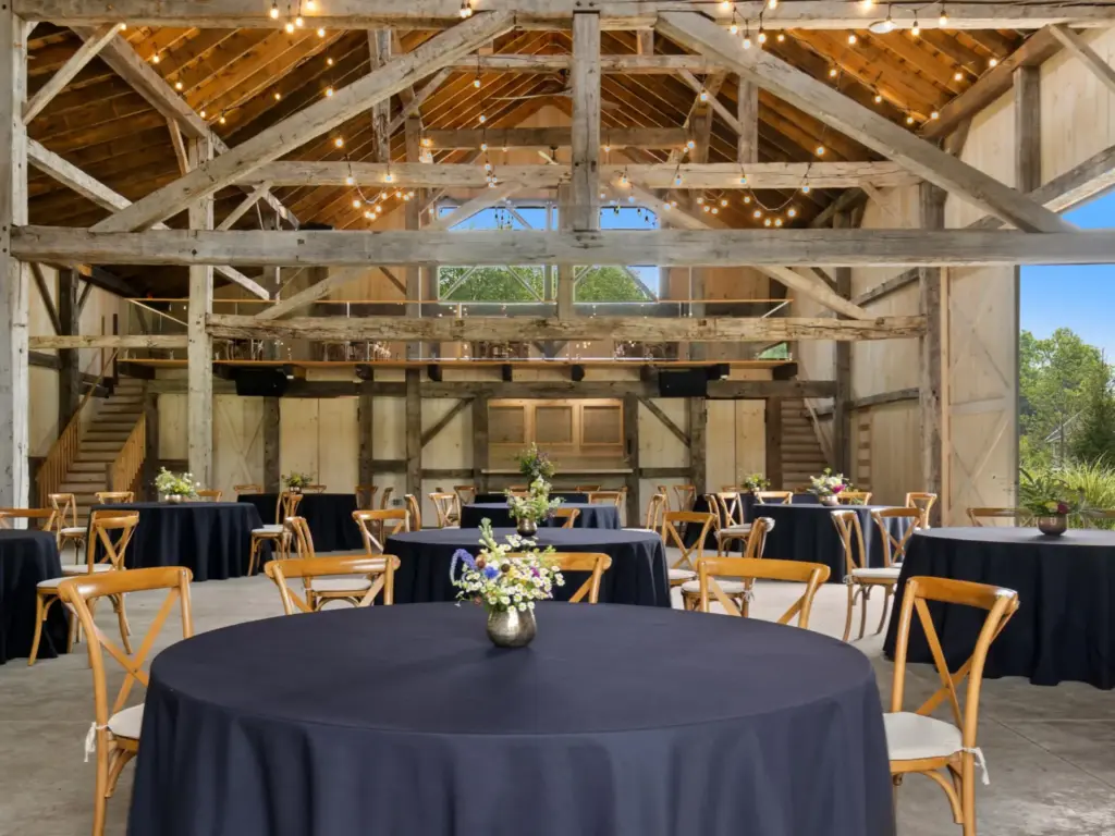 Rustic barn event venue with round tables, navy linens, floral centerpieces, wood cross-back chairs, and string lights.
nature immersive corporate offsites
