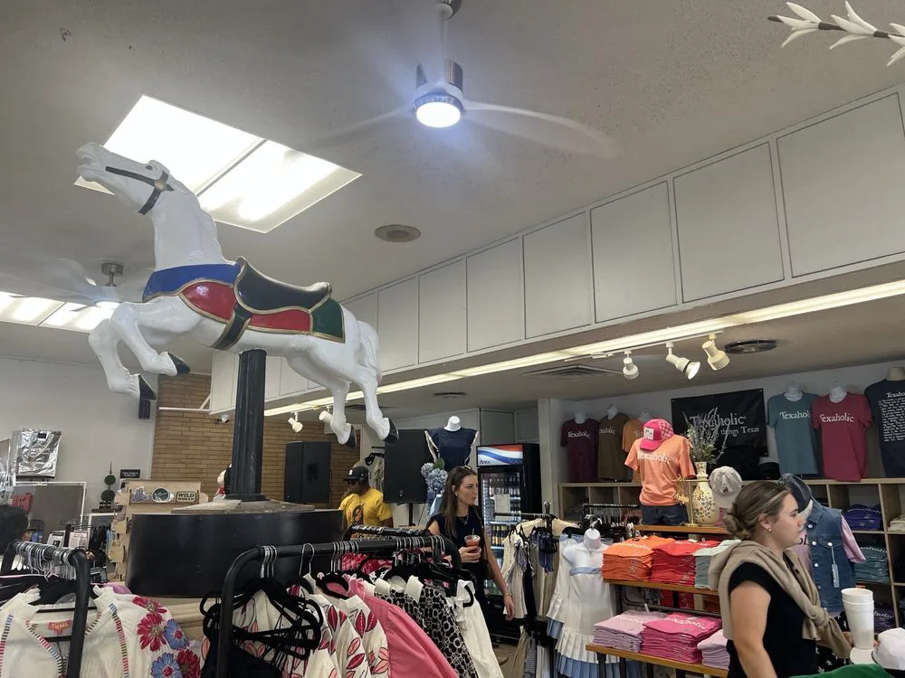 Carousel horse sculpture above clothing racks in a Fredericksburg TX shop displaying Texaholic branded shirts.