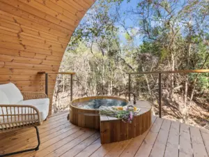 Circular wooden soaking tub on a cedar deck at design-forward nature retreats, overlooking a wooded forest with a rattan chair nearby.