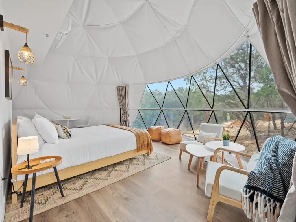 Interior of a geodesic dome tent with a bed and large windows, an ideal glamping choice for where to travel in august.