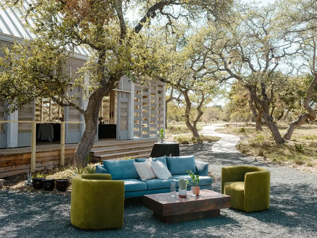 Outdoor lounge area with a blue sofa and green armchairs outside a modern wooden building at The Cedars Ranch.