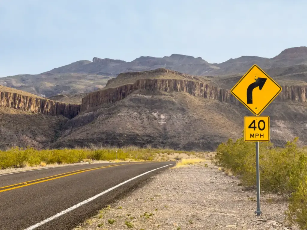 Yellow curve warning sign on one of the best road trips in Texas, a desert highway with a 40 MPH advisory and mountain cliffs ahead.
