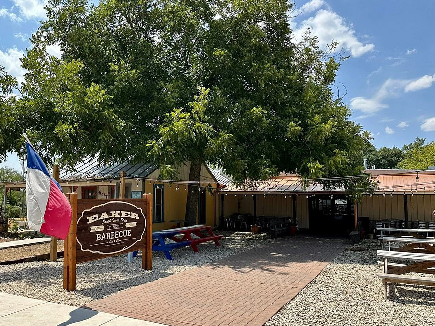 Exterior of Eaker Barbecue, one of the best restaurants in fredericksburg tx, featuring picnic tables under a large tree.