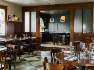 Dining room with green and white checkered floor, dark wood chairs, set tables with wine glasses, and a bar area beyond.