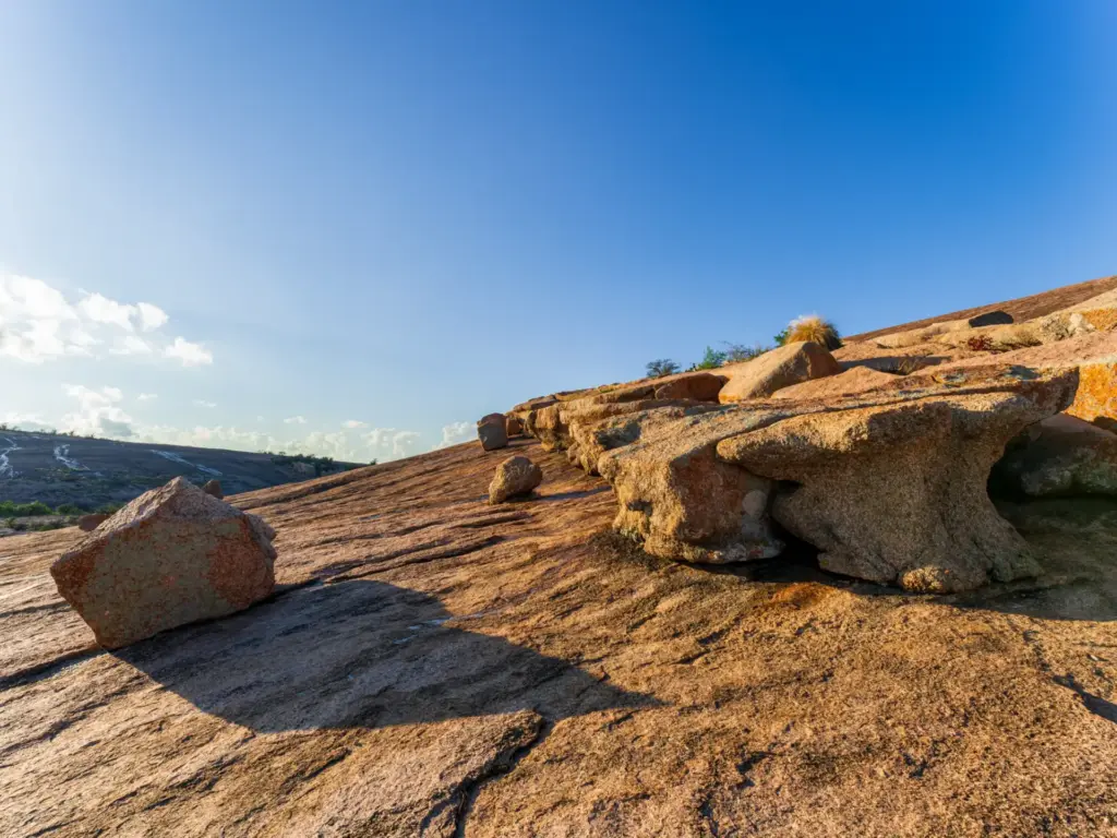 Granite boulders scattered across a sunlit rocky slope under a clear blue sky.
