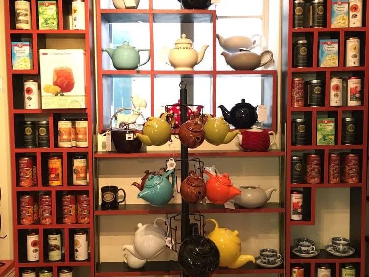 Colorful ceramic teapots and loose-leaf tea tins displayed on red shelves in a shops in fredericksburg tx specialty store.