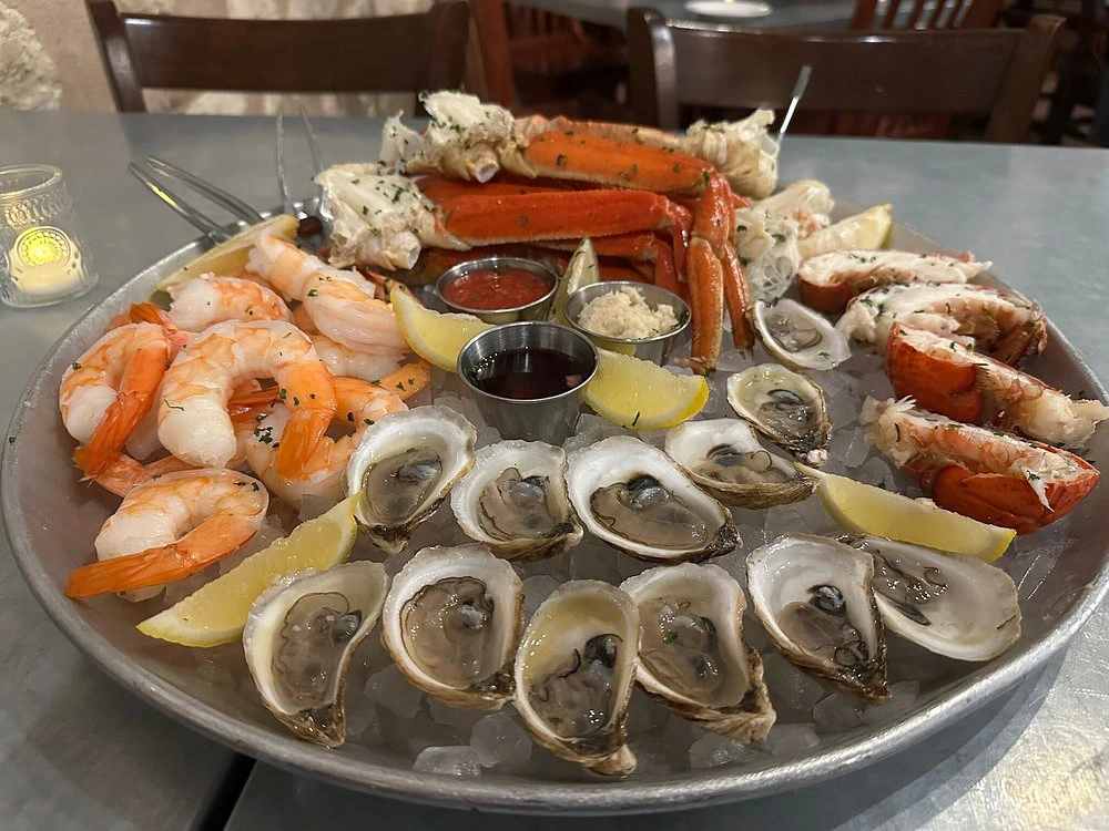 A large chilled seafood platter filled with crab legs, shrimp, oysters, and lobster tails served on ice.
