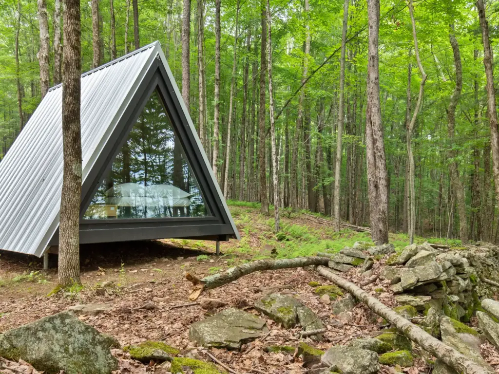 A-frame cabin with triangular glass facade among tall trees, showcasing design-forward nature retreats in a lush forest setting.