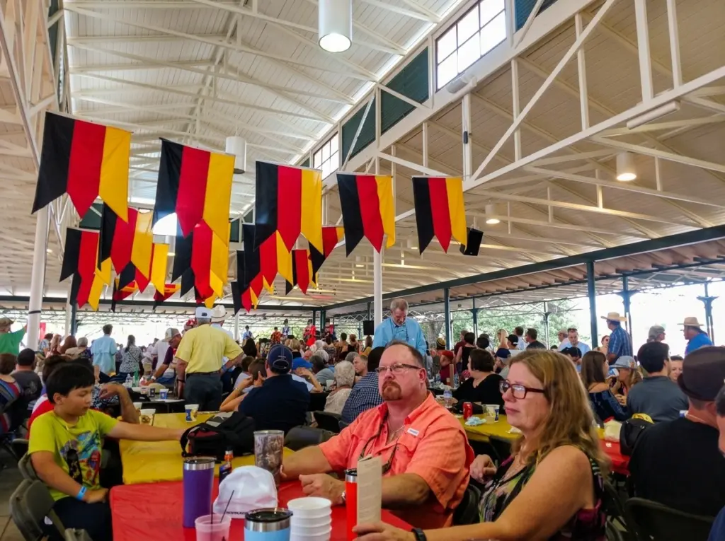 Attendees sit at long tables under German flag banners during a festival.