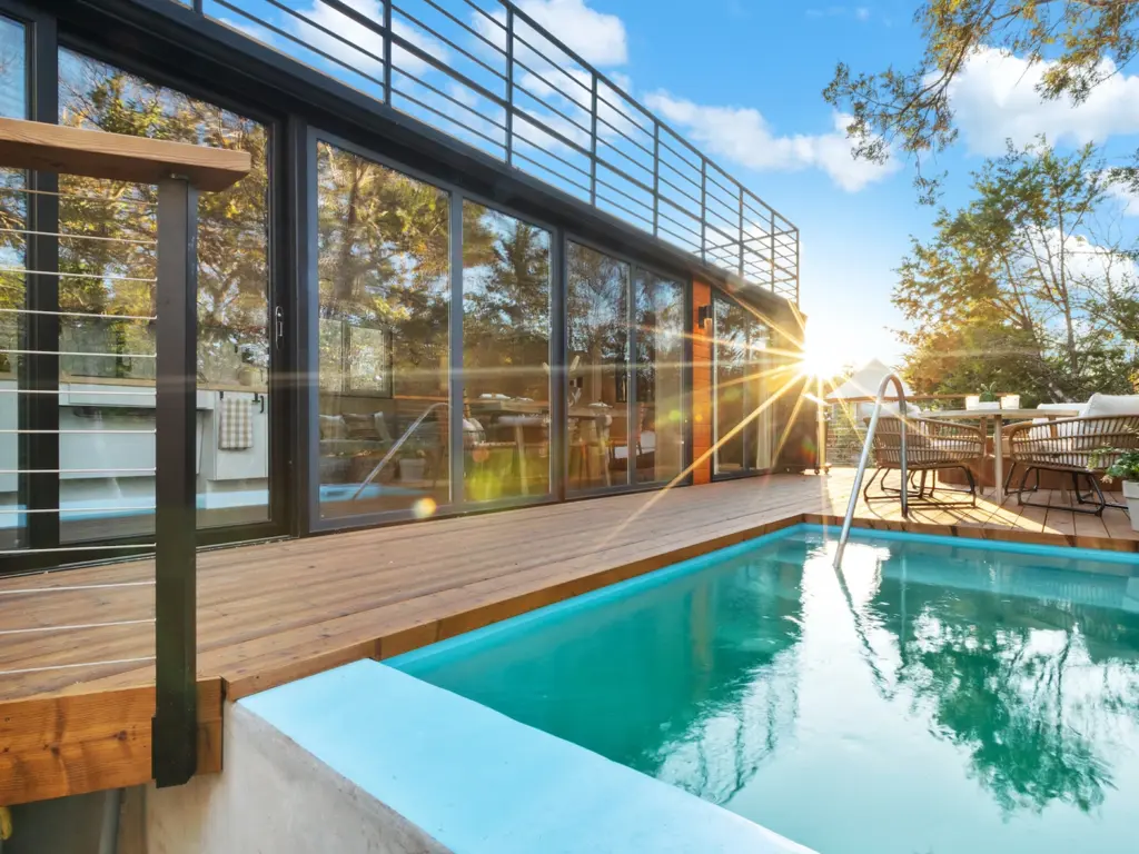 A private plunge pool on a wooden deck outside a modern cabin with large sunlit glass doors at Onera.