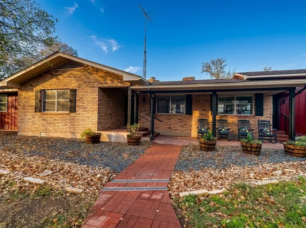 A single-story brick house featuring a covered front porch with rocking chairs and a brick walkway.