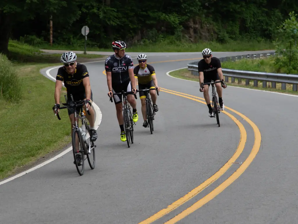 Four cyclists riding road bikes together around a curve on a paved mountain road.